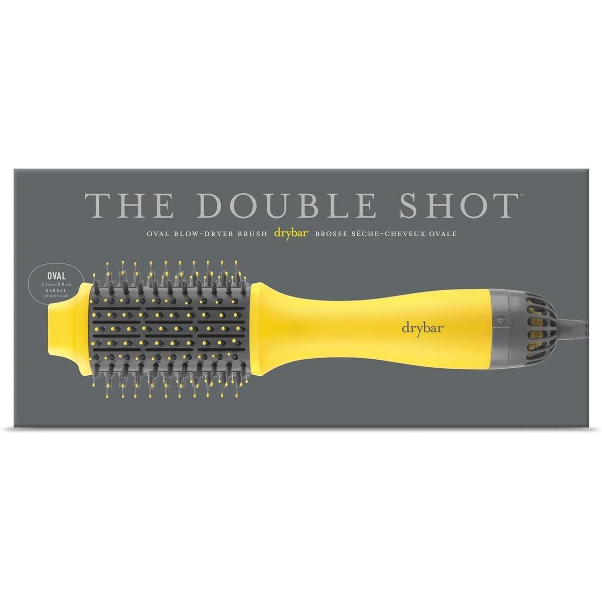 Drybar Double Shot yellow oval blow-dryer brush with tufted bristles in its grey product packaging.