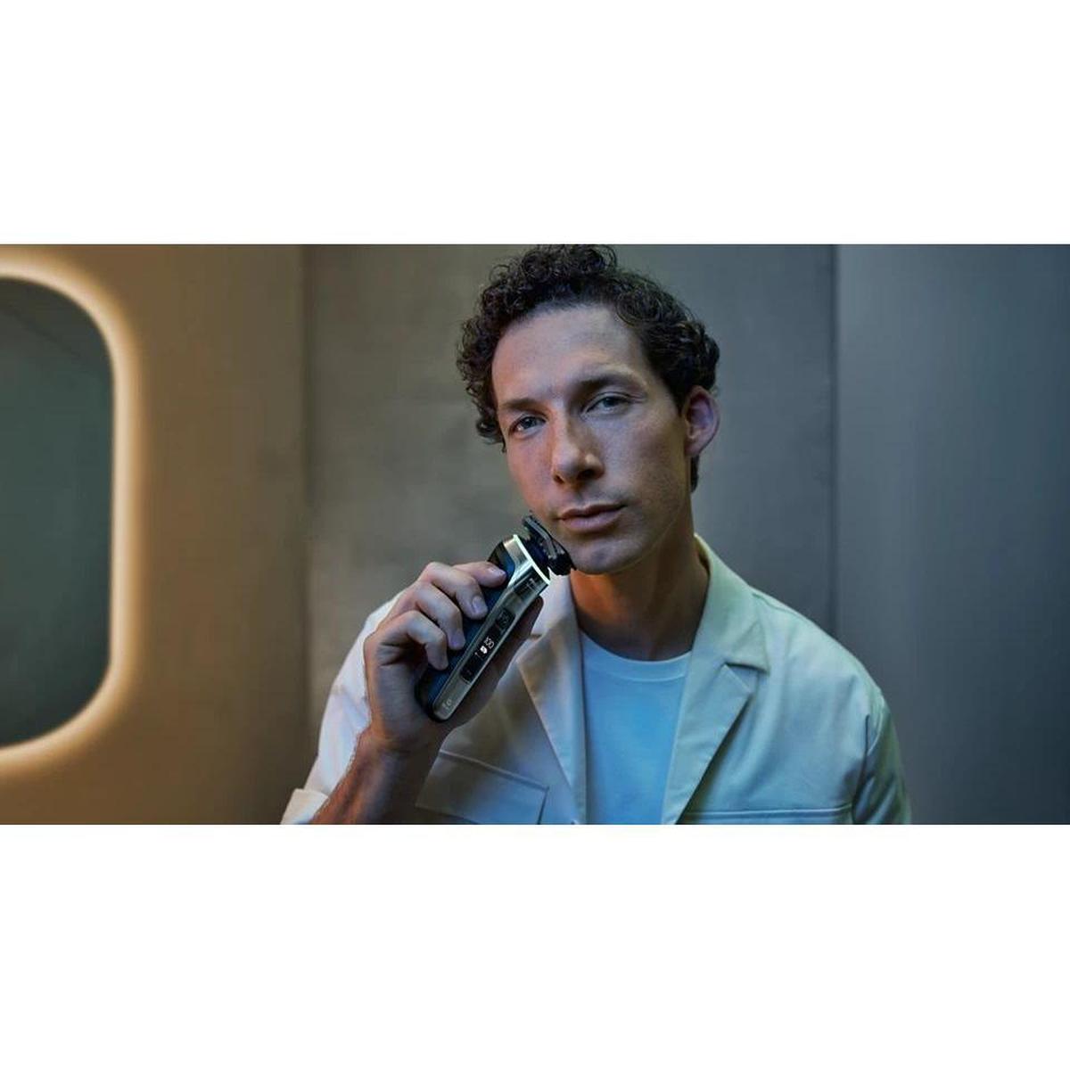 Man using a sleek, silver and black Philips Series 9000 electric shaver with a digital display in a modern bathroom.