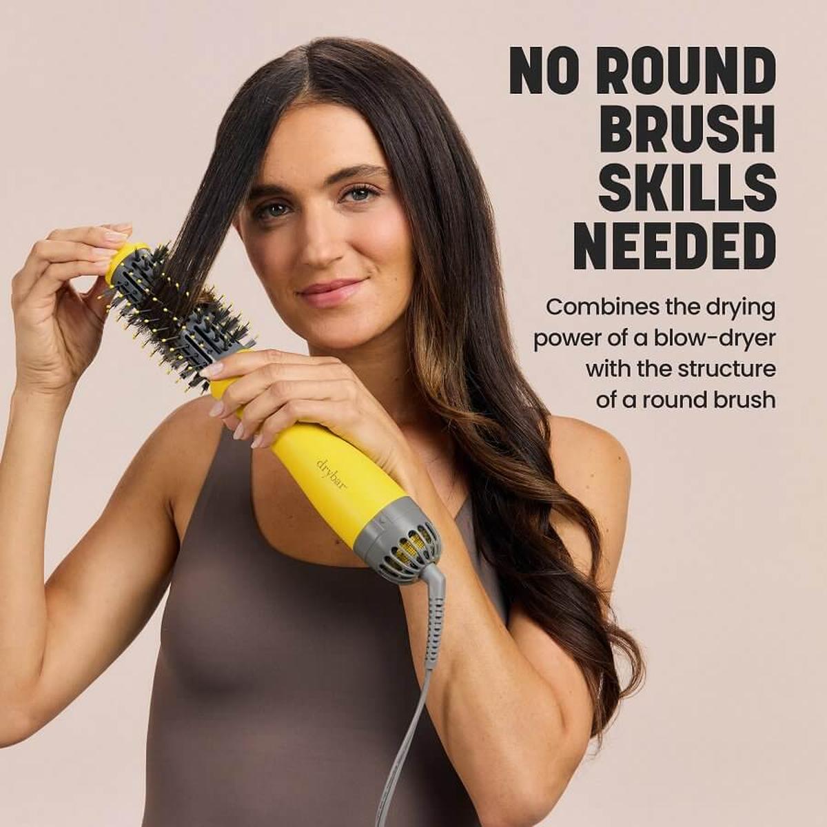 Woman styling hair with a yellow Drybar Half Shot 3.8cm round blow-dryer brush featuring nylon and tufted bristles.