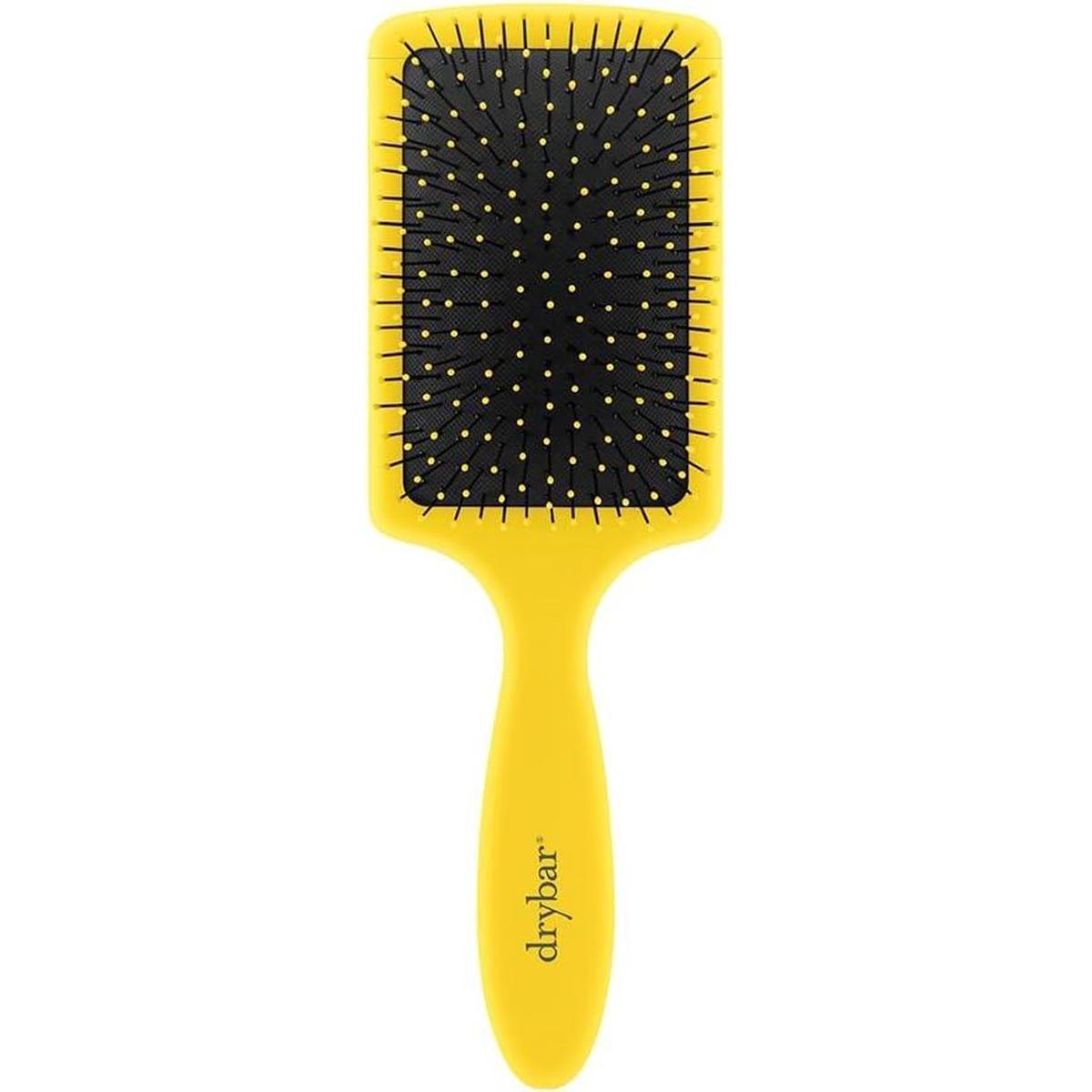 Drybar yellow paddle brush with a soft-touch finish, black cushioned base, and flexible nylon bristles for detangling.