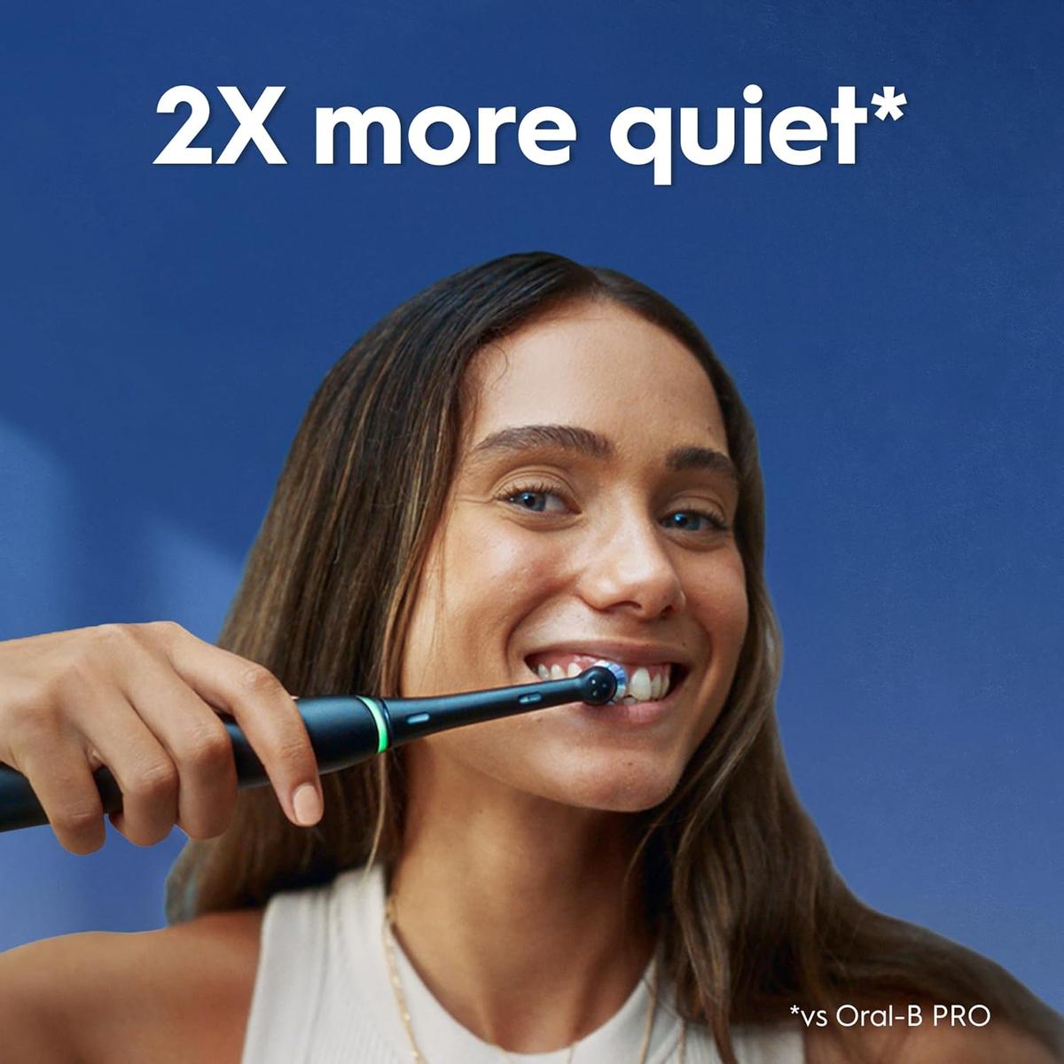 Woman smiling while using a sleek black Oral-B iO9 electric toothbrush against a blue background with 2X more quiet text.